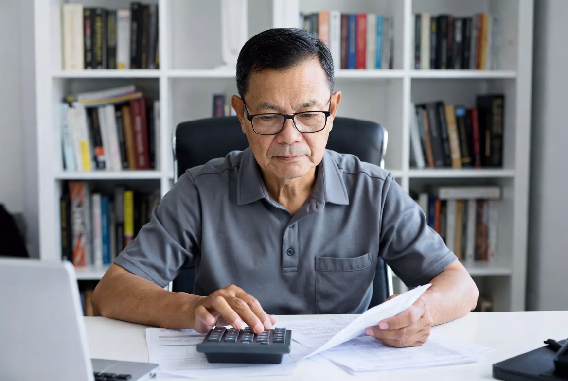 A male investor using a calculator alongside tax documents in a home office